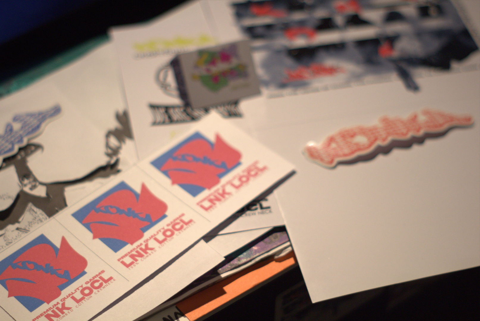 LNK LOCL sticker sheets and printed artwork laid out on a table